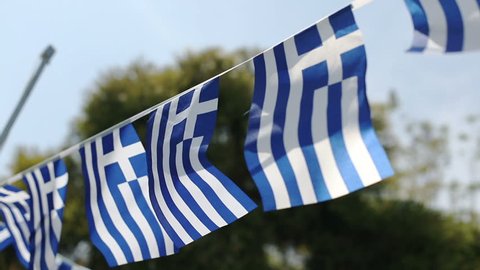 A string of small Greek flags fluttering in the wind against the sky in slow motion.