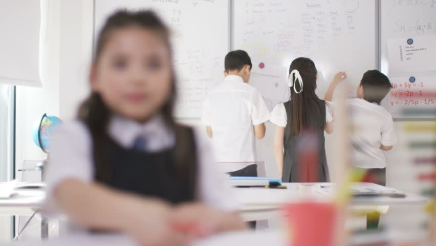 4K Portrait little girl at her desk in classroom with friends in background UK - April, 2016