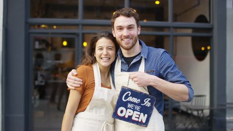 4K Happy owners outside cafe hold up a sign to show they are open for business. UK - April, 2016
