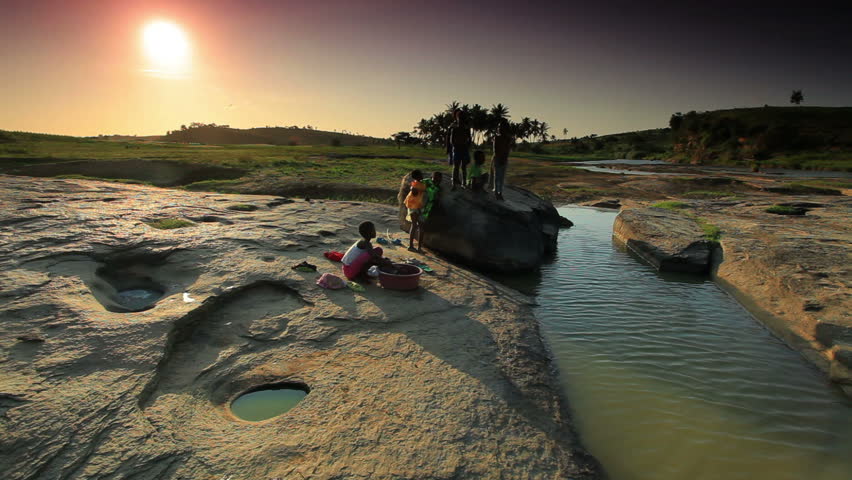 Kids wash clothes in river under sunset in Africa