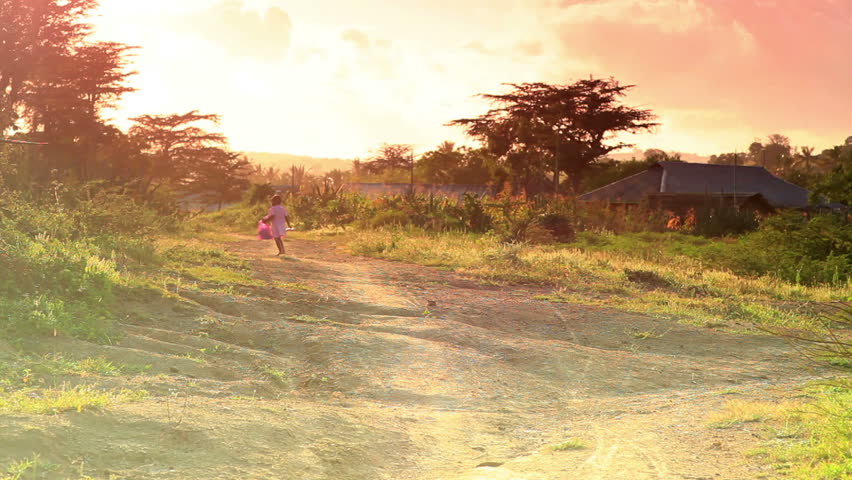Little girl in pink dress runs along dirt road in Africa