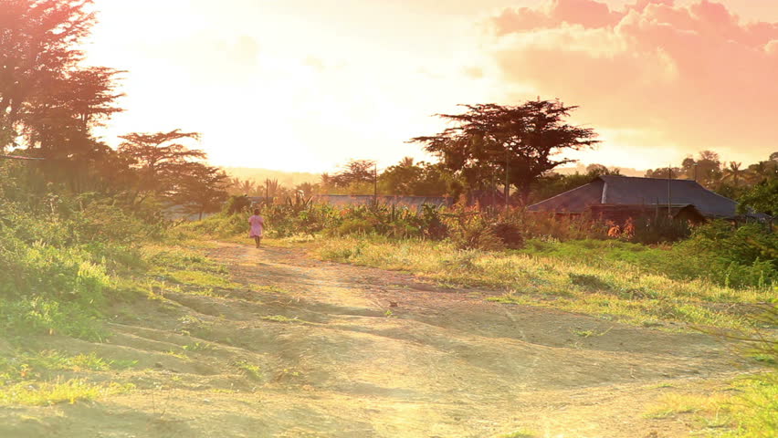 Little girl in pink dress runs along dirt road in Africa