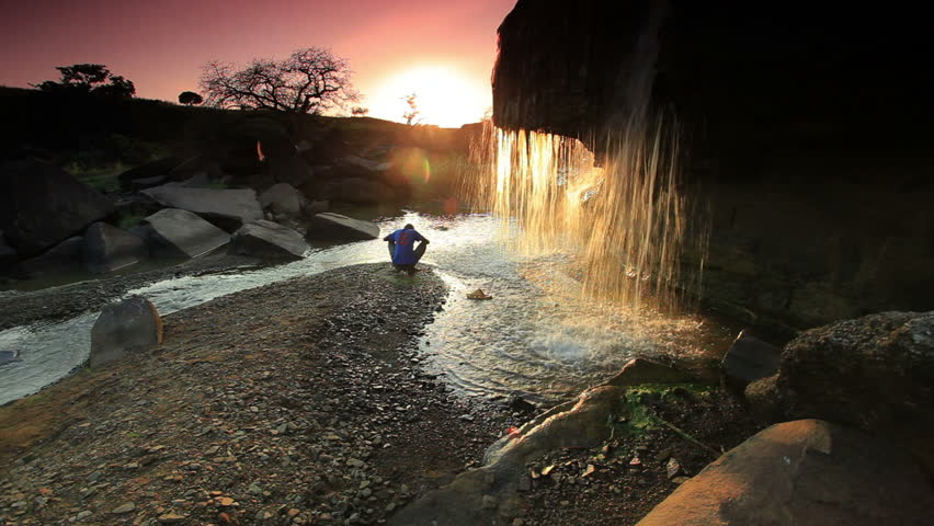 Child watching a waterfall and tossing a rock at sunset in Kenya, Africa.