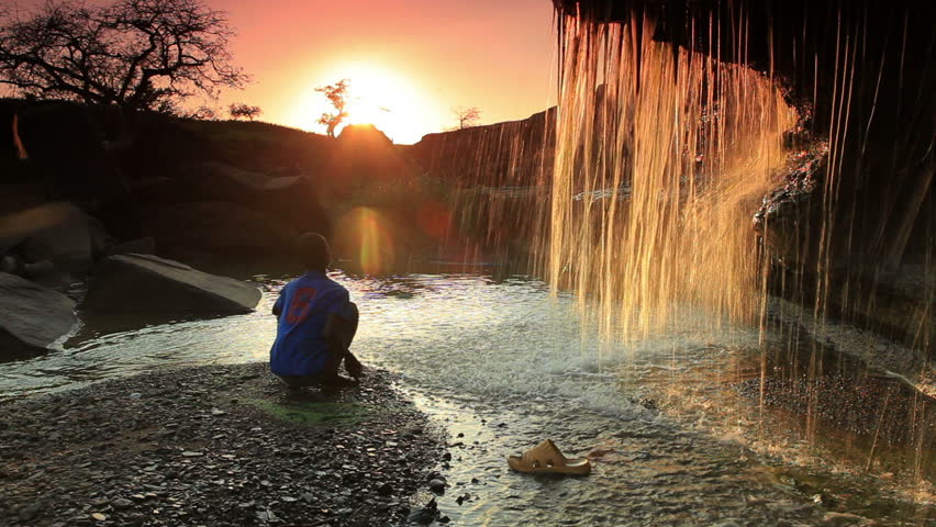 KENYA, AFRICA - CIRCA AUGUST 2010: Child watching a waterfall and tossing a rock