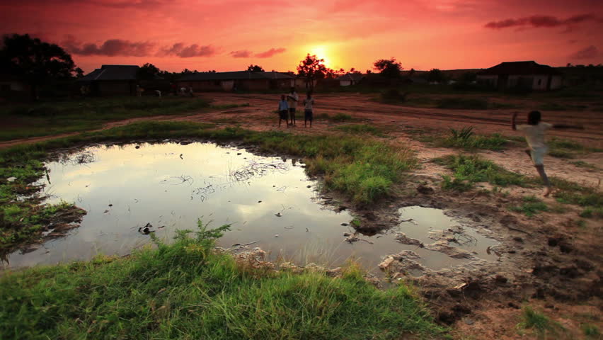 Group of boys play at village water hole at sunset in Africa