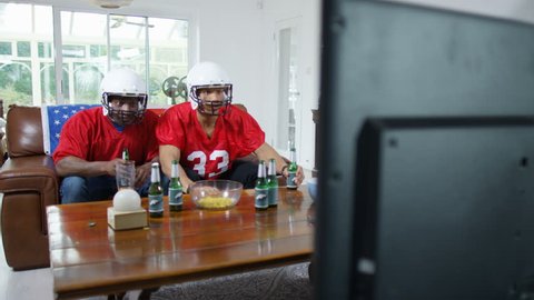 4K 2 friends hanging out together & watching American football game on TV UK - April, 2016: stockvideo