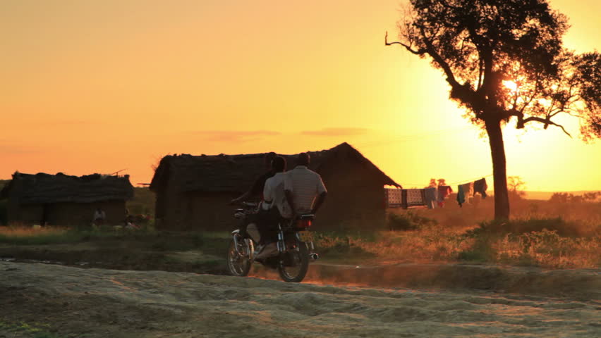 Three people riding past on a motorcycle at sunset in Kenya, Africa.