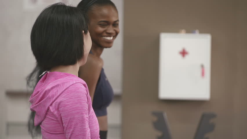 Couple of young dark skinned  African-American and Asian women doing fitness exercise work out with dumbbells in gym