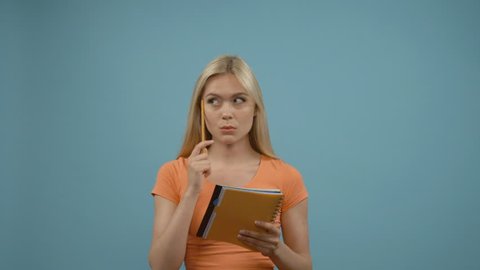 Girl got an idea. Beautiful young blonde woman in orange top pointing away and making notes while standing against blue background.
