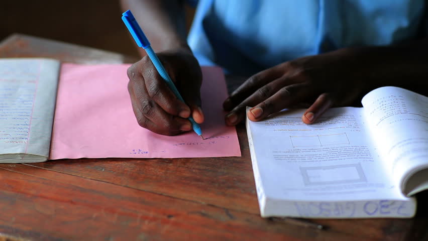Close up on hands of school boy doing homework after school in Kenya, Africa.