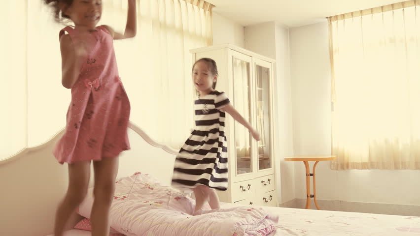 Happy children jumping and dancing on bed with warm window light