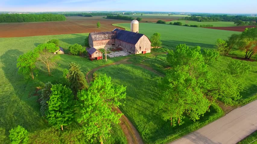 Rustic abandoned farm amid lush, scenic springtime landscape of agricultural fields, aerial view.