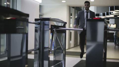 The businessman is passing through a turnstile. A man in a jacket and white shirt opens turnstile via card and comes into a business center.