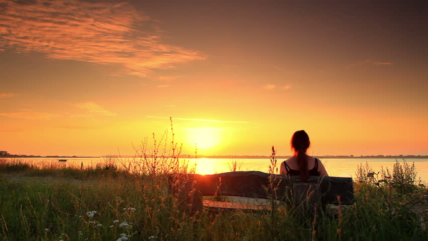 Woman sitting on a bench outside looking out at the sea at sunset in Copenhagen,