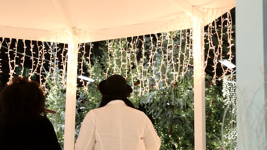 Two women singers singing Christmas songs standing in white gazebo near decorated Christmas trees