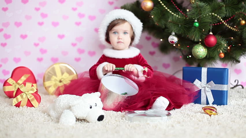 Baby girl with xmas gifts on the floor. The girl sitting next to a Christmas