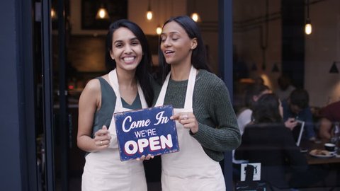 4K Happy women outside cafe hold up a sign to show they are open for business UK - April, 2016