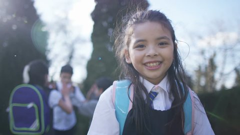 4K Portrait of smiling little girl with backpack, outdoors in school playground UK - April, 2016
