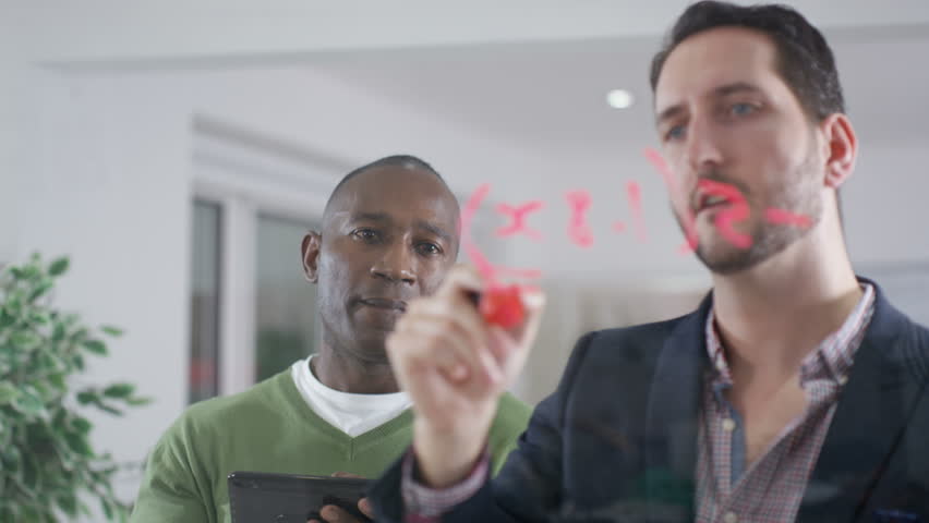4K Businessmen brainstorming for ideas, writing math formula on glass screen. Shot on RED Epic. UK - April, 2016