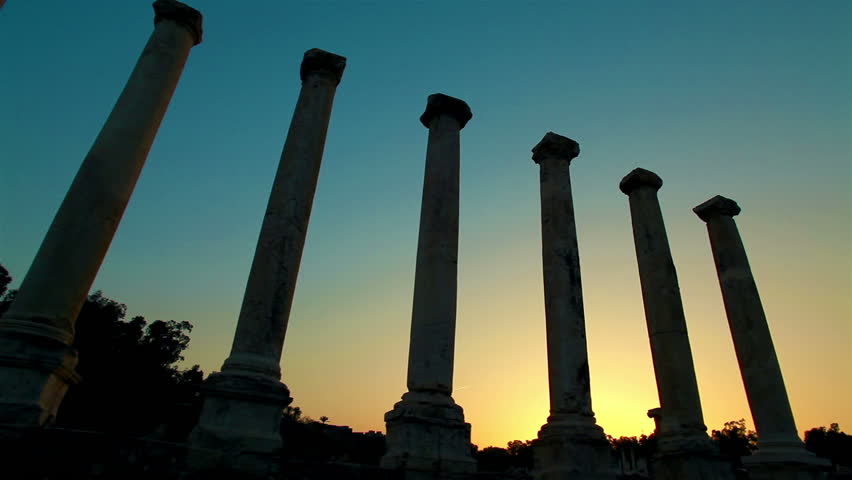 Low angle slider dolly move across seven silhouetted columns at sunset at the
