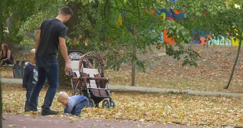 Opole/poland - Oct 04 2015: Man, Father, Dad With His Sons, Boys Are Playing at Park Throwing up Dry Leaves From the Ground, Baby Pram, People Are Walking, Woman is Sitting at the Bench, Men Women