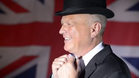 British businessman, turns to face camera, adjusts his bow tie then winks, whilst the Union Jack blows in the background.