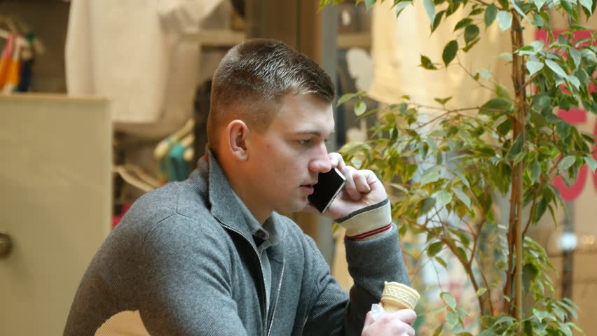Young handsome talking on the cellphone and eating ice cream in the cafe in shopping mall. Close-up