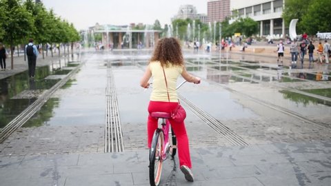 Woman on pink bike are not daring to go through jet of dry fountain in Muzeon park on Crimean embankment.