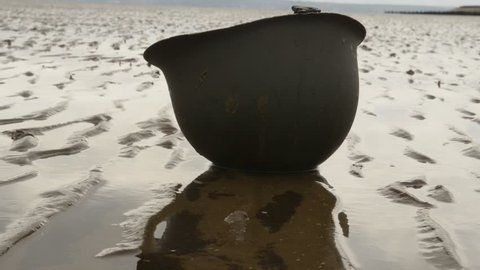 D-Day Landings - American WW2 helmet lies upside down on beach at low tide, with a slight breeze causing ripples on the pools of water.