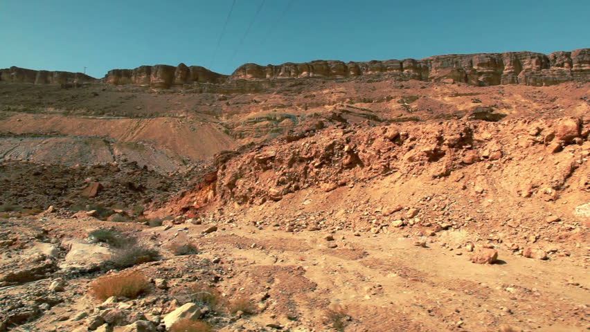 Wide drive-by of the Mitzpe Ramon Crater desert floor and cliff face in Israel.