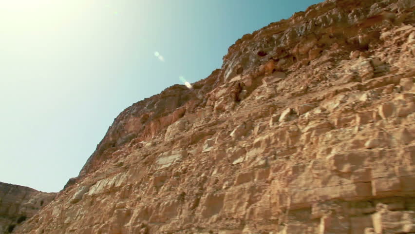 Medium wide, close-up drive-by of the desert cliff face from the bottom of the
