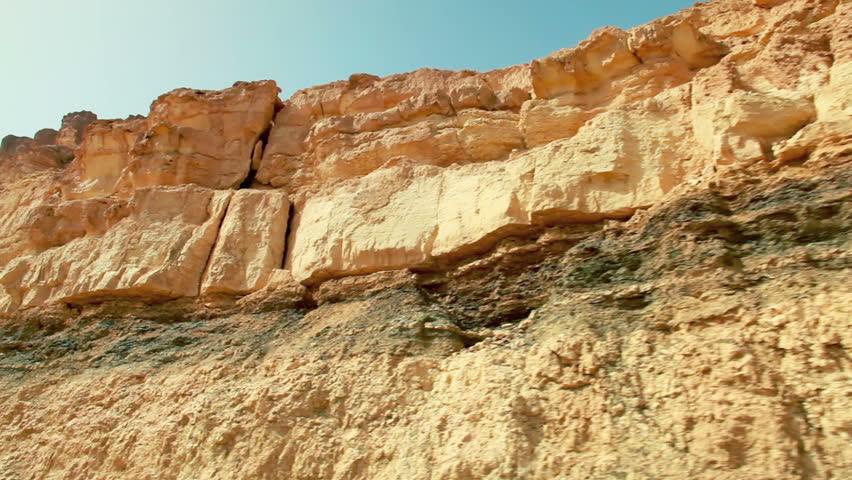 Medium wide, close-up drive-by of the desert cliff face from the bottom of the