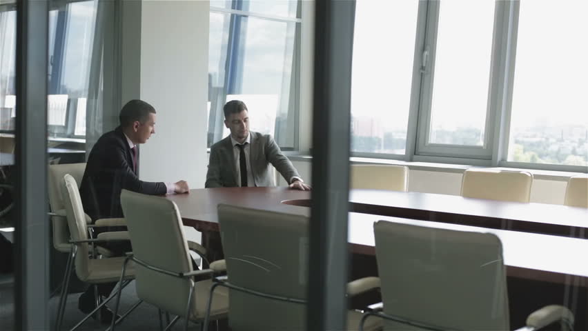Two businessmen are sitting at a table in a room behind a glass wall. Businessmen in suits are discussing new project in a meeting room. | Shutterstock HD Video #17057164