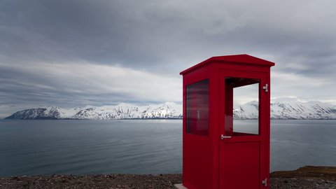 4K Timelapse tilt shot of a red phone booth in the middle of nowhere with snow covered mountains in the background in Iceland