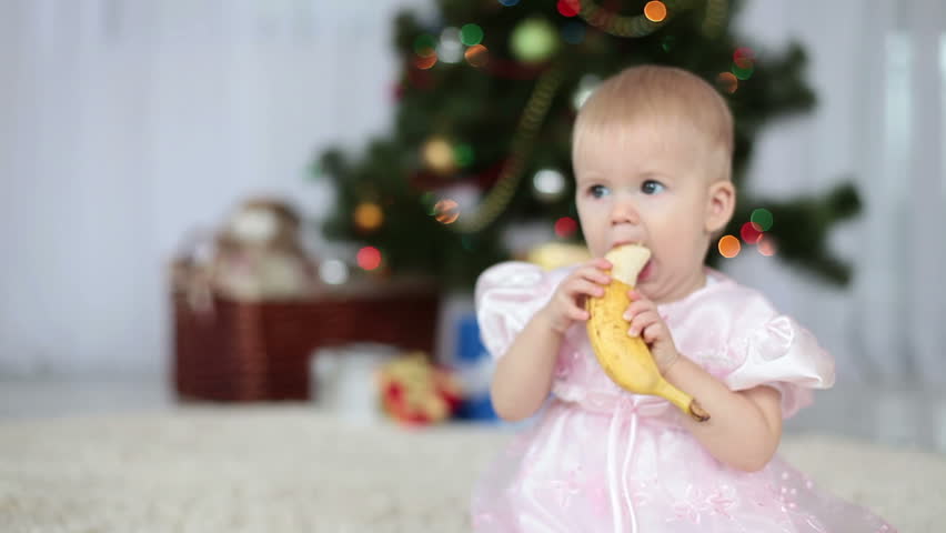 Little girl eating a banana on the background of the Christmas Tree