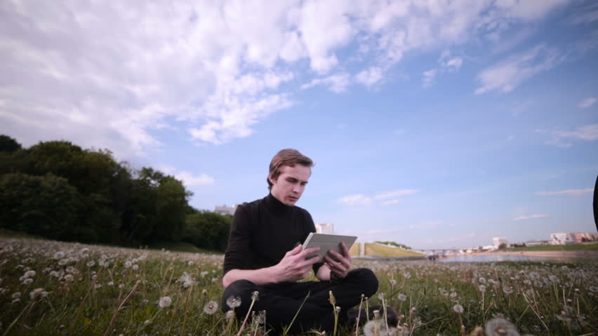 Young man with tablet computer sitting in the park, chatting, surfing, studing.