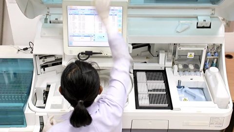 Woman working in laboratory on modern machine for blood testing. Medical staff works machine with display for control blood. Doctor at hospital checked sample in machine above view. Analysis of blood.