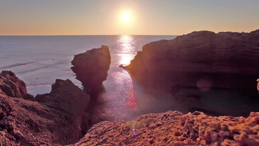 Orange sunset at Dor Beach in Israel. Pocked rock formations on the shore, and the sun setting into the Mediterranean Sea.
