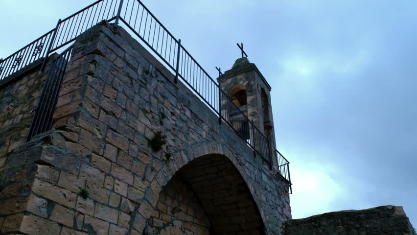 A tilt down from the bell tower of an ancient church, to an arched alcove with