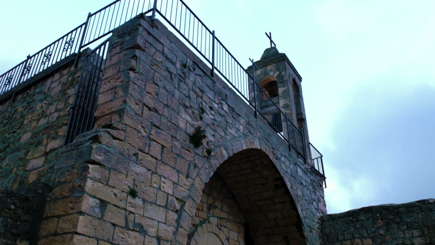 A tilt down from the bell tower of an ancient church, to an arched alcove with