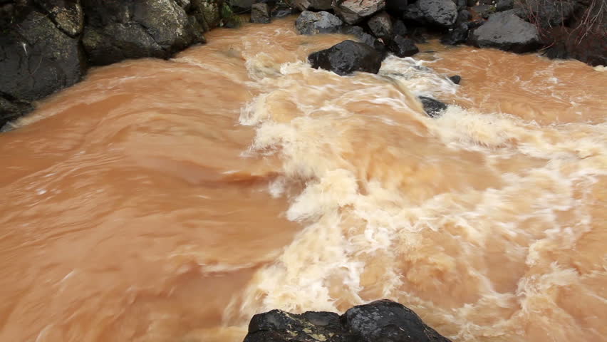 Close-up of a small, turbulent rapid of muddy water at a river in the Golan