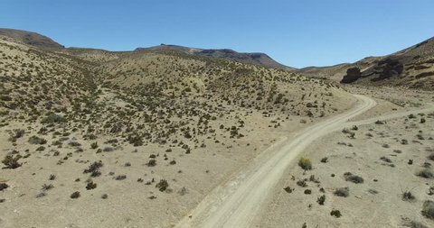 Aerial scene of dirt road in dry, desertic, mountainous landscape. Car, appears traveling,is lost behind a close hill. High perspective of dry panorama. Patagonia, argentina, Chubut, Piedra Parada. 