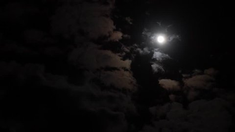 Clouds pass by a full moon in the nightime sky