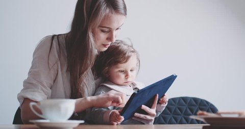 Young Caucasian Mother using Tablet with her Baby Daughter. Slow Motion 120 fps 4K DCi. Mother showing her Child digital Tablet. Children and Technology concept. Toddler girl. Cinematic family