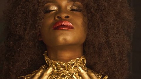 Magic surreal golden african american female model with bright glitter makeup, glossy golden hairstyle and big red lips
