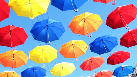 Multicolored umbrellas hanging over head on the street against the blue sky and swinging in the wind