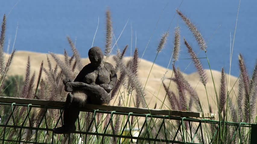 Small human statue sitting on a fence overlooking the Dead Sea at Ein Gedi