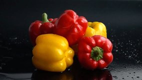 Water pouring on yellow and red peppers in slow motion again black background