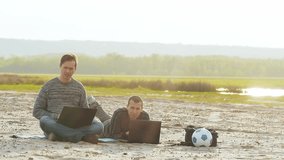 Two men working on the beach with a laptop slow motion video