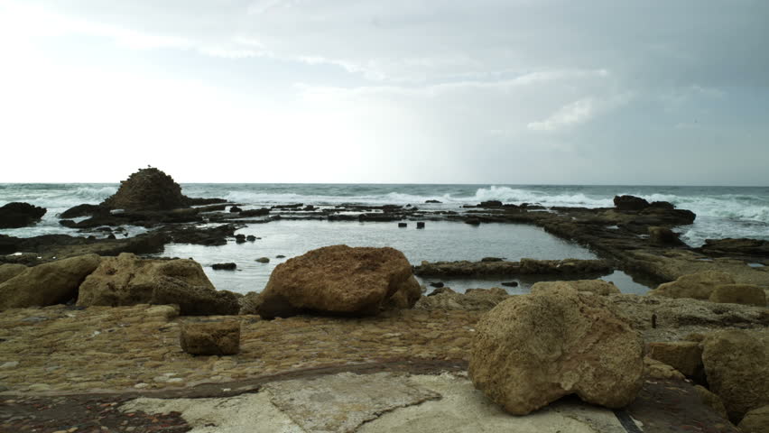 Wide shot of waves rolling over outcrop of remaining partial ruin at Ceasarea